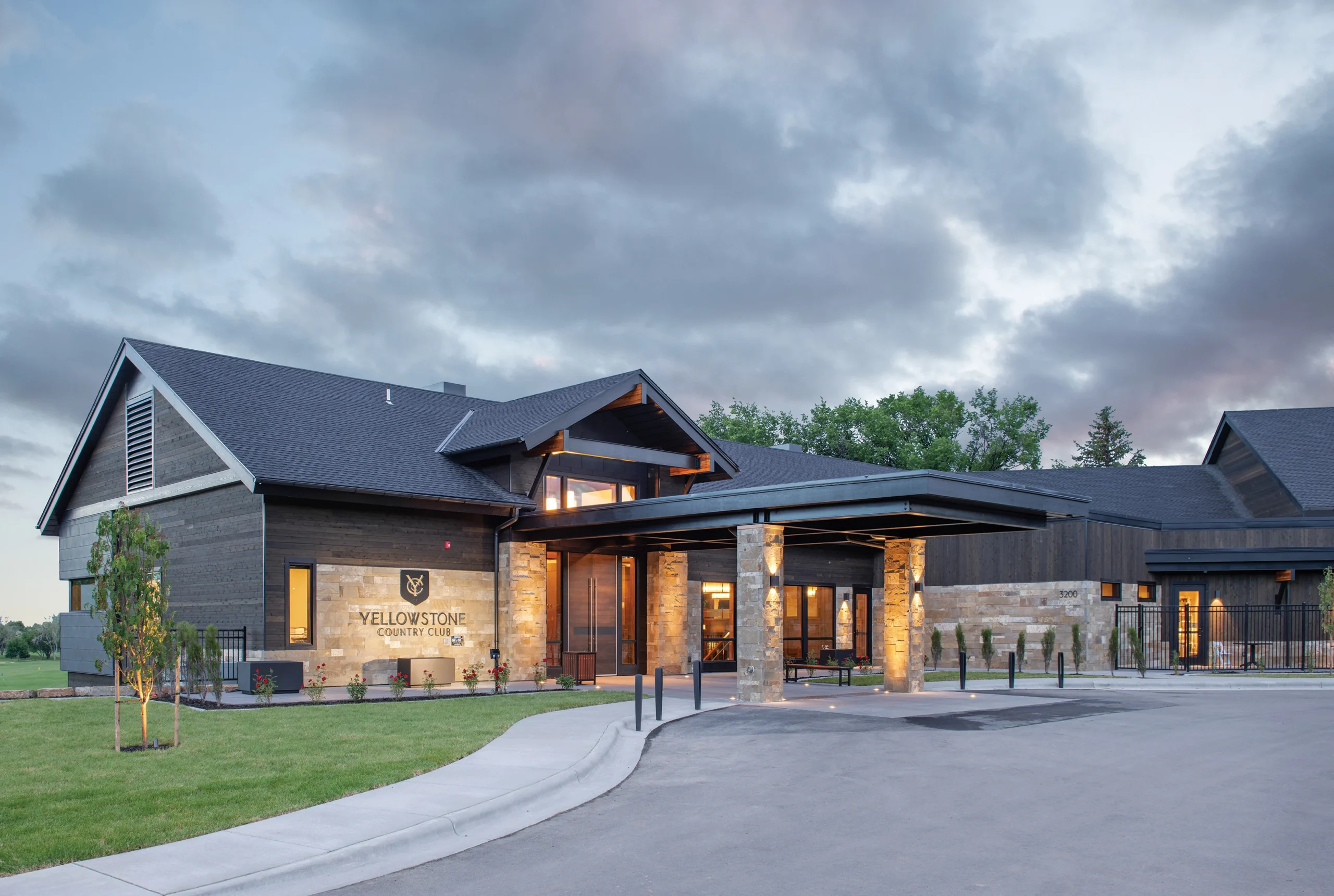 Exterior view of Yellowstone Country Club's clubhouse featuring rustic stone and wood architecture, illuminated pillars, and a modern entrance under a dramatic sky.