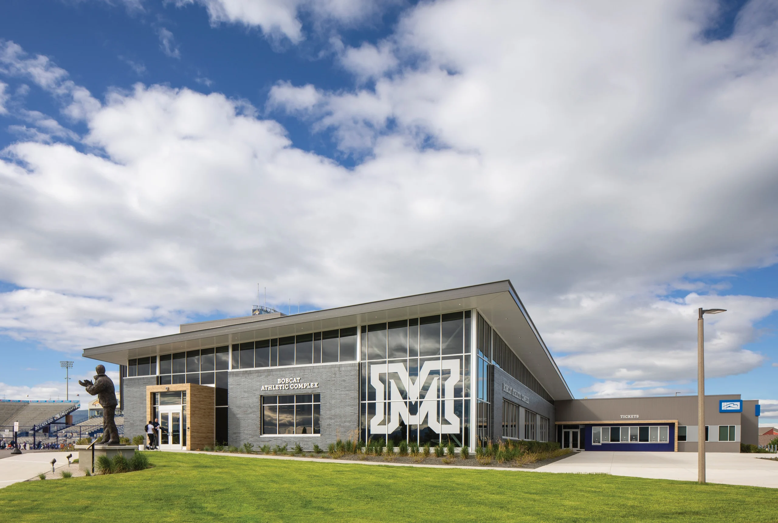 The exterior entry of MSU Bobcat Athletic Complex, featuring a modern façade with expansive glass windows, bold university branding, and a welcoming entrance adjacent to the stadium.