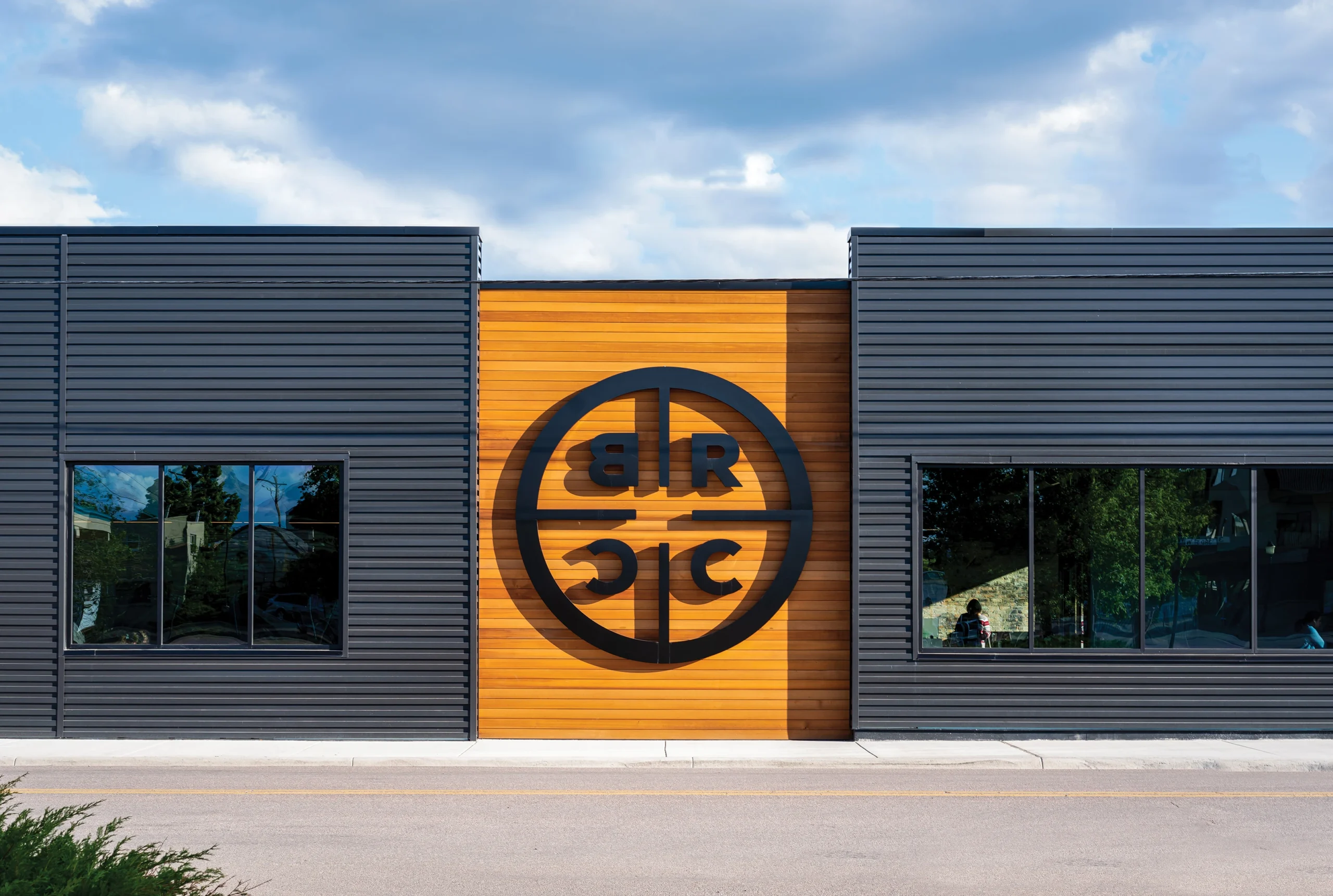 Exterior of Black Rifle Coffee Company’s Kalispell Outpost, showcasing a bold black logo on a warm wood facade framed by sleek black metal siding, reflecting the brand’s rugged, military-inspired aesthetic.