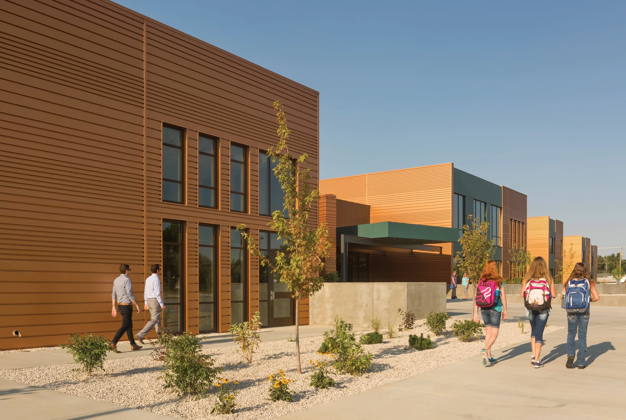 The exterior of Medicine Crow Middle School features a modern, linear architectural design with warm earth tones, sustainable landscaping, and shaded walkways, creating a welcoming environment for students and the surrounding community.