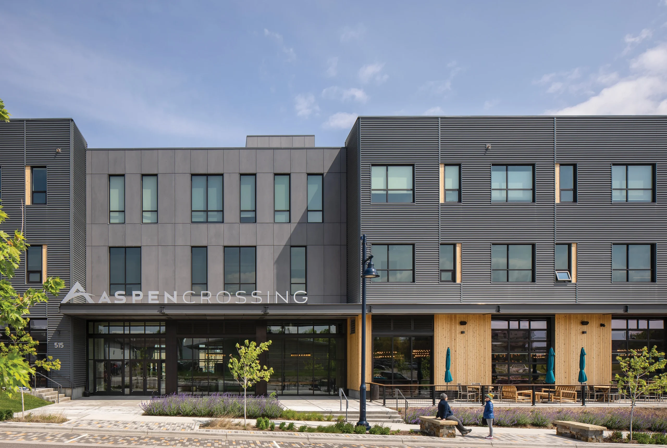 The Aspen Crossing entrance showcases a pedestrian-friendly plaza, warm wood accents, and modern metal cladding.