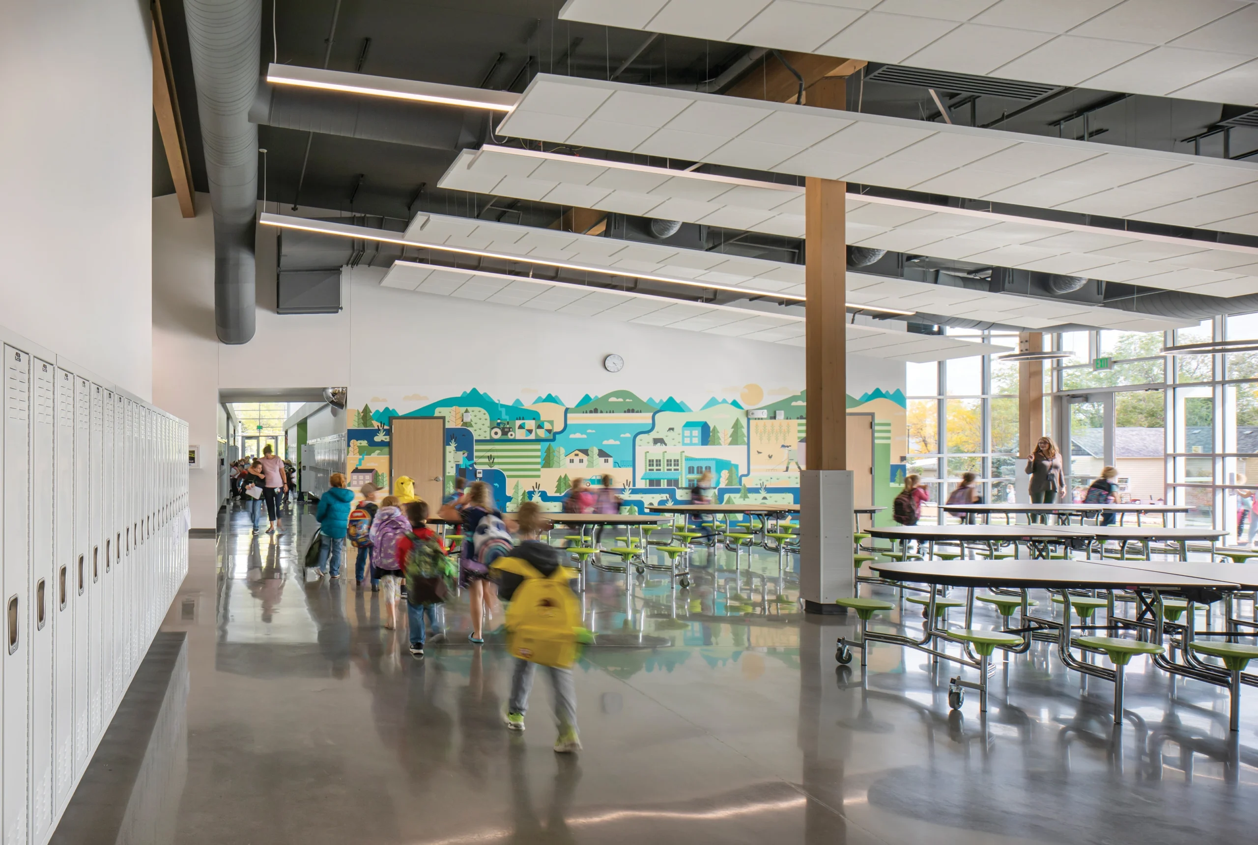 The cafeteria at Columbus Elementary School showcases experiential graphic design with a vibrant, educational mural that reflects the local landscape, enhancing the modern space with visual storytelling and creating an engaging environment for students.