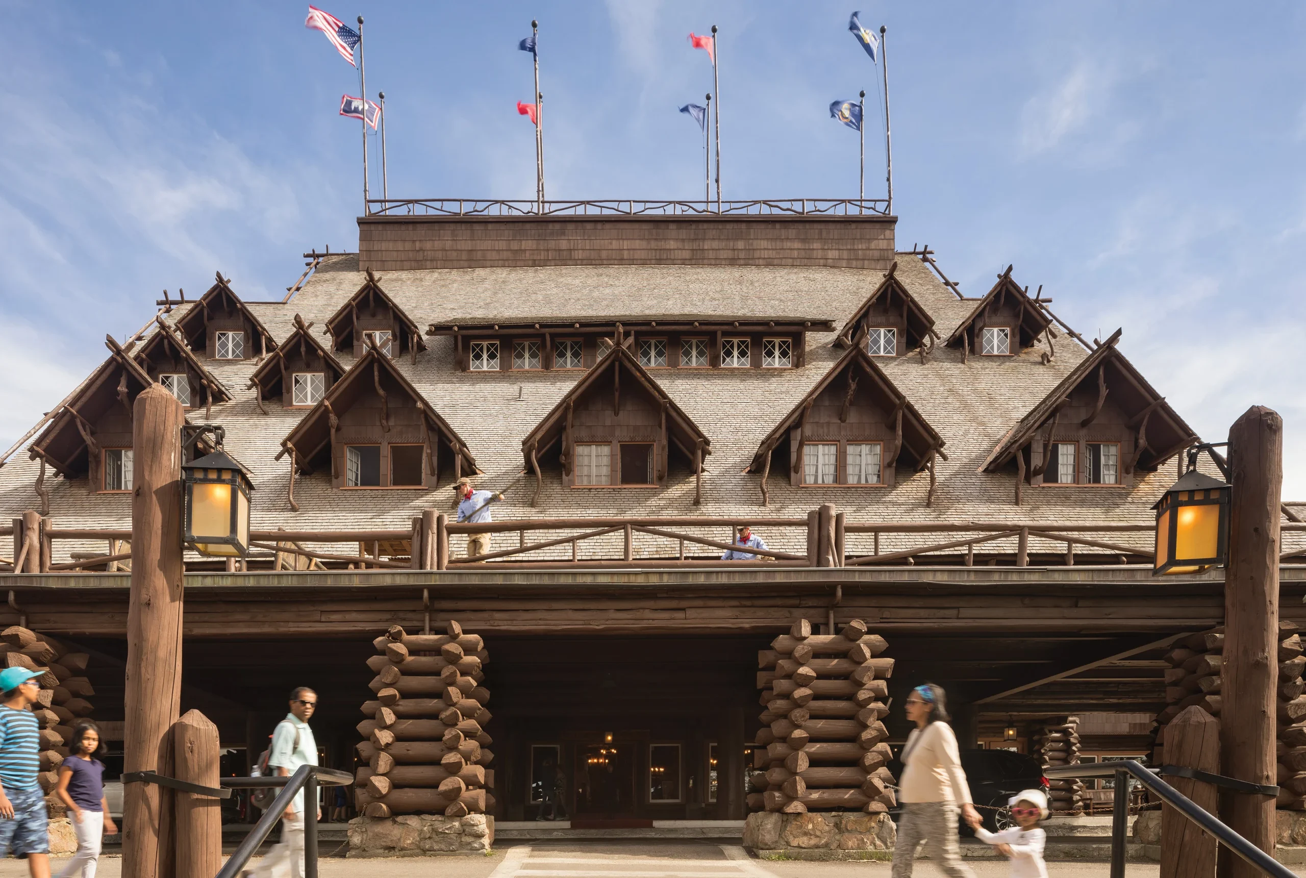 Close-up view of Old Faithful Inn’s intricate log architecture featuring steep gabled windows, rustic railings, and timber construction, with visitors and staff enhancing the scene.