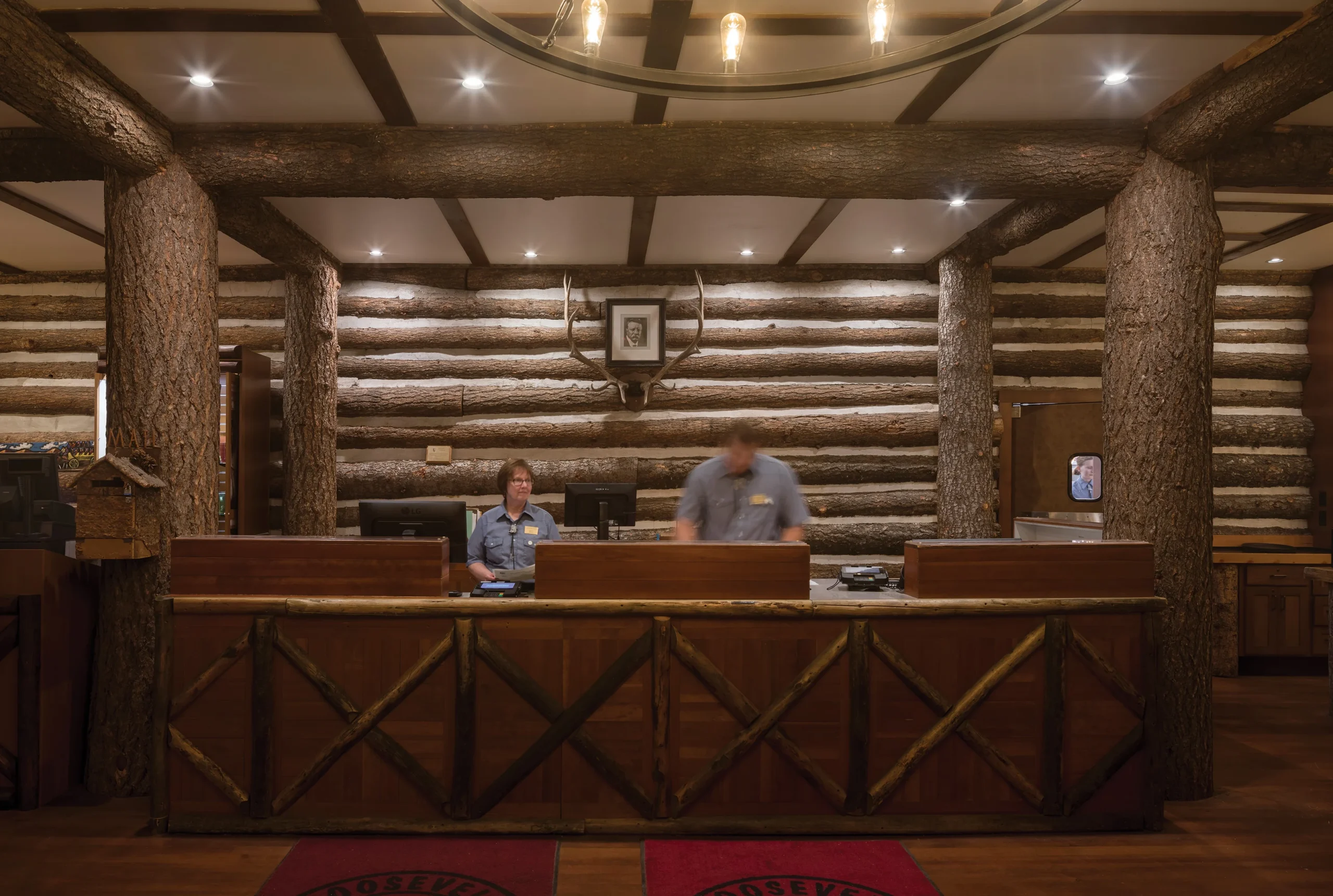 Rustic reception area of Roosevelt Lodge showcasing thick log columns, textured log walls, and a polished wooden desk with natural wood detailing.