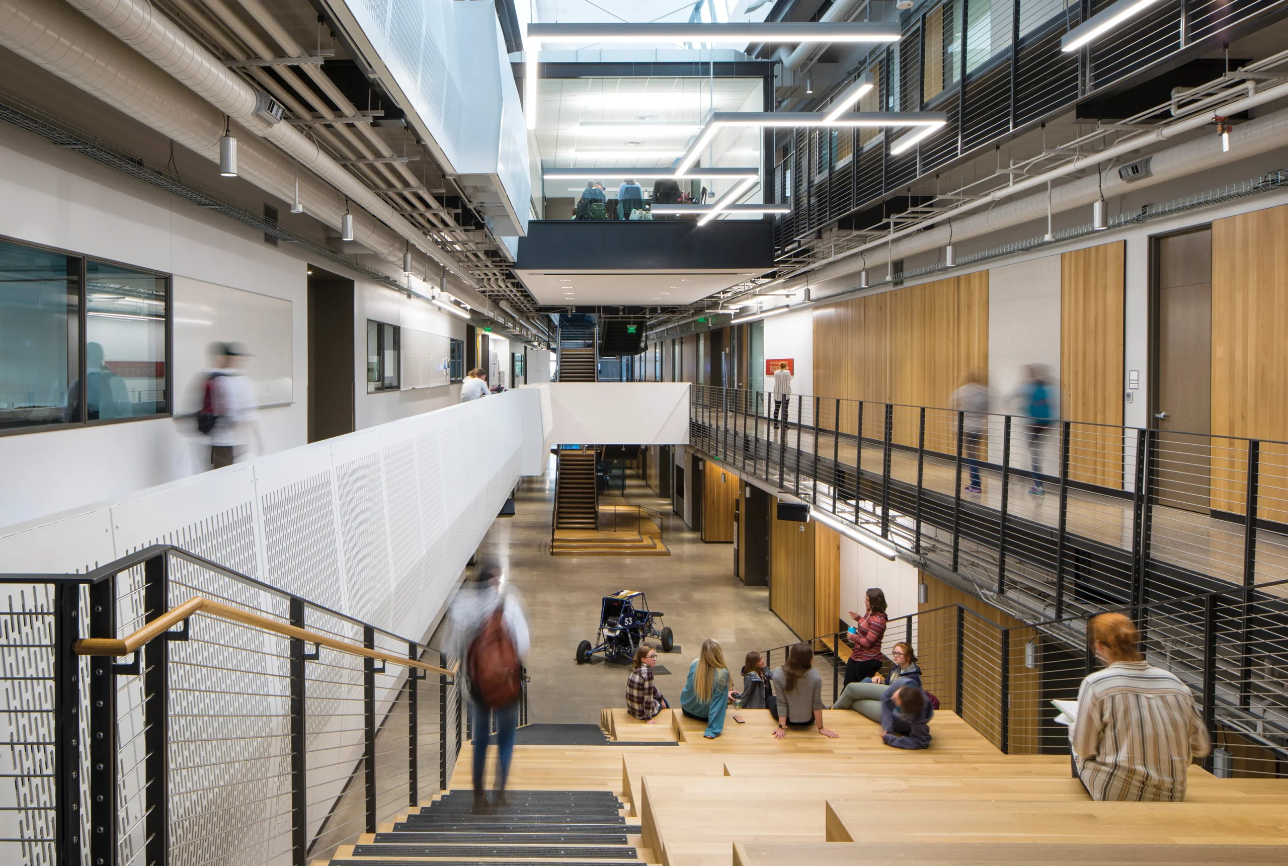 An interior view of MSU Norm Asbjornson Hall, highlighting a multi-level collaborative learning space with warm wood finishes, open walkways, and students engaging in hands-on education.