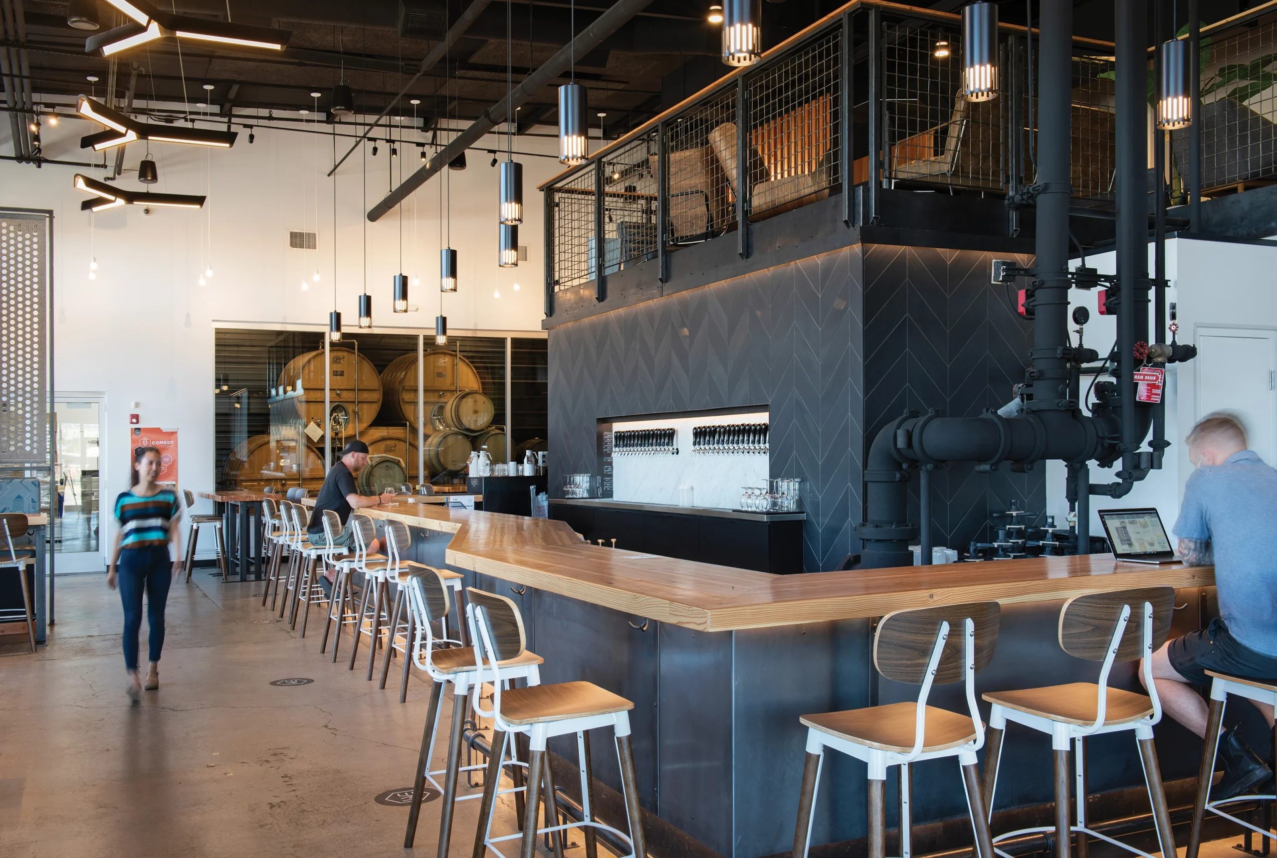 By All Means brewery's design blends wood, metal, and concrete with warm lighting and communal seating, creating an inviting atmosphere that celebrates craft brewing and fosters guest connection.