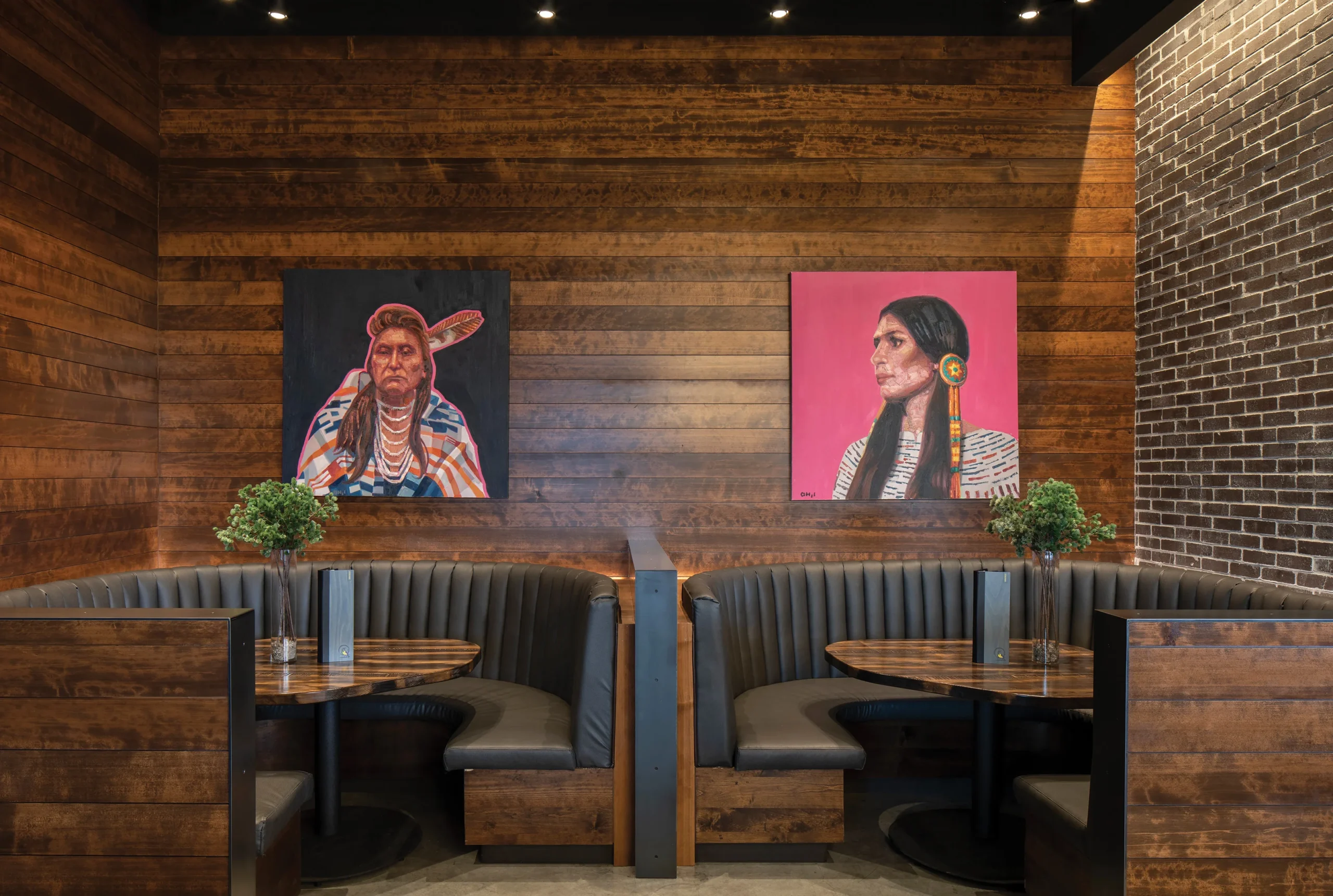 Curved leather booths with wood tables set against a warm wood-paneled wall featuring vibrant Native American portraits, creating an intimate dining space.