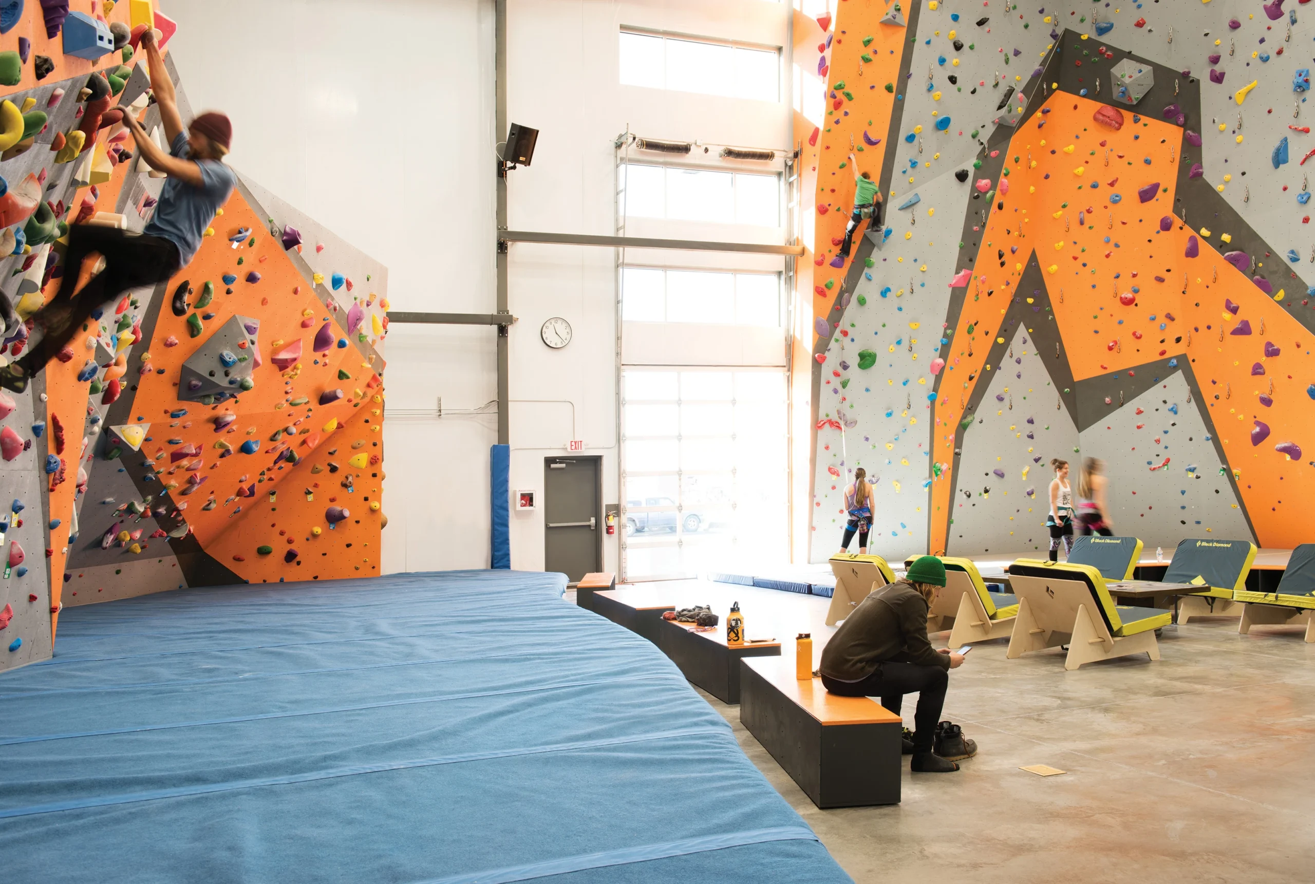 Interior of SteepWorld Climbing & Fitness featuring a dynamic bouldering wall, towering rope climbs, and a lounge area for climbers to rest and connect.