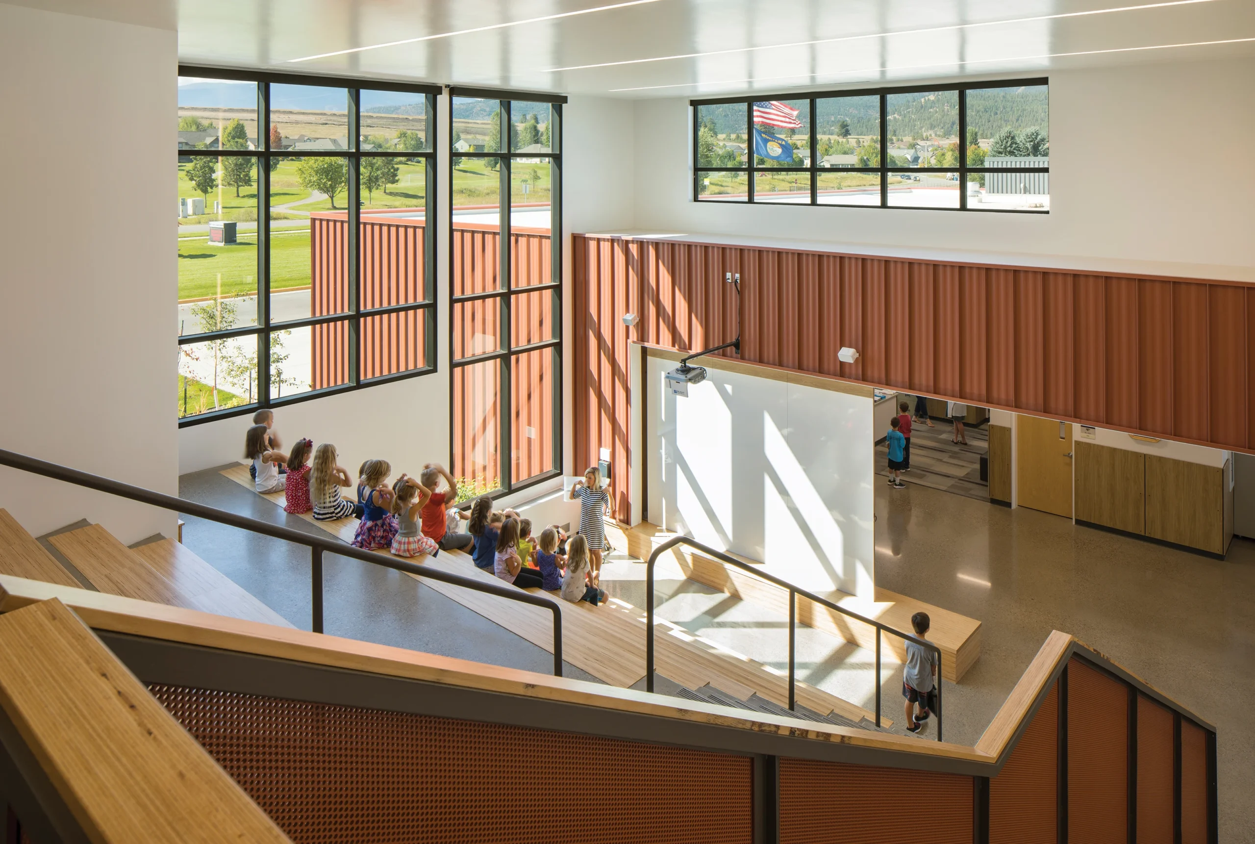 A bright and welcoming learning stair at Jeannette Rankin Elementary School features tiered seating, large windows that invite natural light, and an integrated projection wall—creating a dynamic, flexible space for group learning and community engagement.