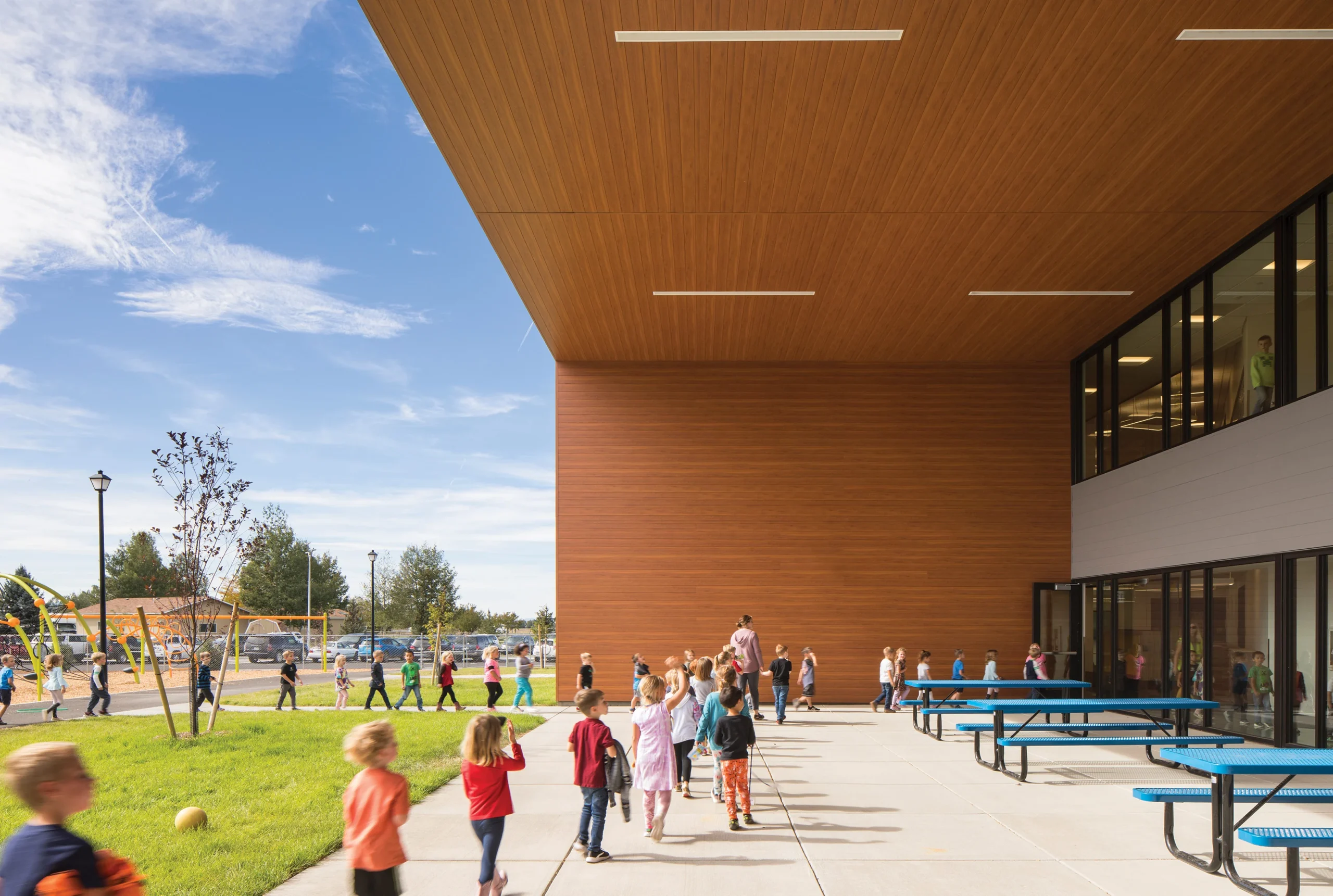 An outdoor learning space at Story Creek Elementary School features modern architecture with wood-clad overhangs, blue picnic tables, and ample room for students to gather and interact.