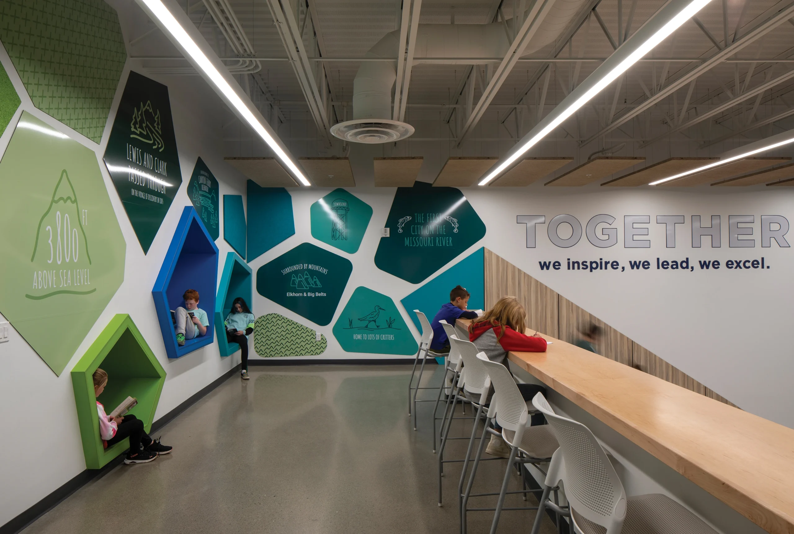 A creative learning space at Townsend Schools featuring colorful, geometric reading nooks, bold environmental graphics inspired by local landmarks, and a collaborative high-top counter.